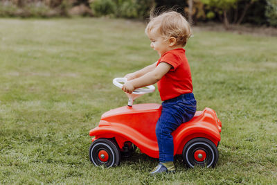 Side view of cute boy riding toy scooter on field