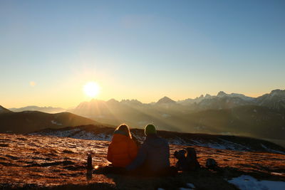 People relaxing by mountains against sky during sunset