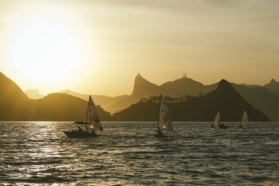 Boats on sea by silhouette mountain against sky during sunset