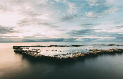 Rock formation amidst sea against cloudy sky during sunset