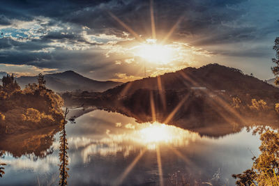 Sunlight streaming through clouds over lake during sunset