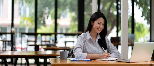 Young woman using phone while sitting on table