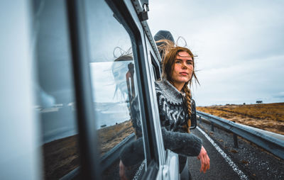 Young woman wearing sunglasses against sky seen through window