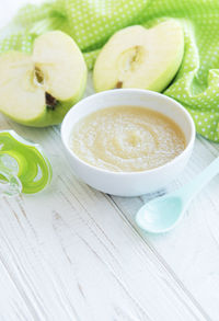 Bowl with baby food and apples on table