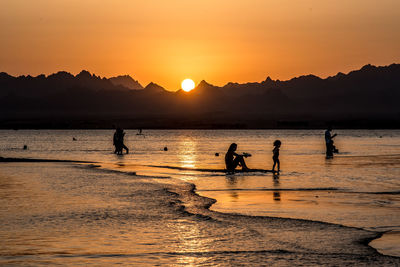 Silhouette people on beach against sky during sunset