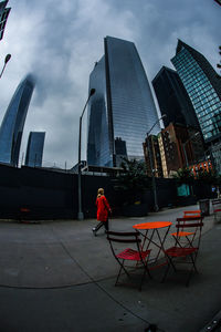 Man walking by modern buildings in city against sky