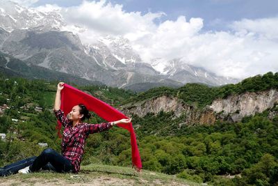 Smiling woman holding red scarf against mountains