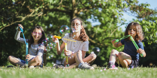 Portrait of three beautiful caucasian girl sisters blowing soap bubbles while sitting in the park