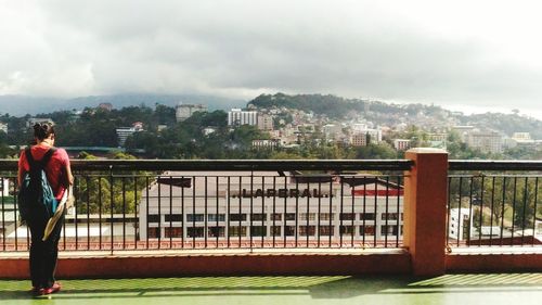 People standing on footbridge in city against sky