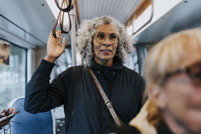 Elderly woman standing in bus while traveling for work