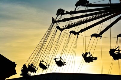 Low angle view of silhouette people enjoying swing ride against sky during sunset