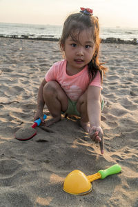 Portrait of cute girl playing on sand at beach during sunset