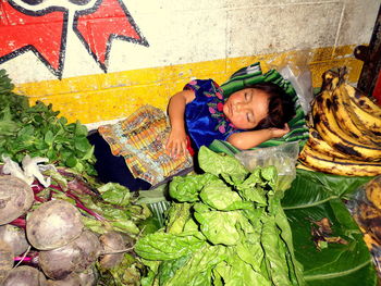 High angle view of girl sleeping by vegetables and fruits at market