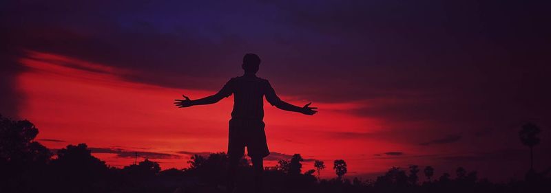 Silhouette man standing on cross against sky during sunset