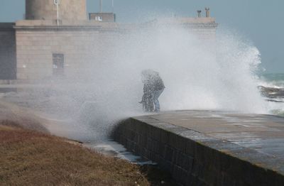 Waves splashing on person standing at footpath