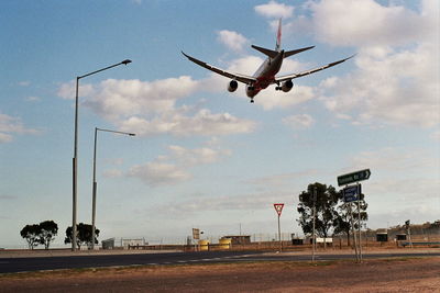 Airplane flying over road against sky