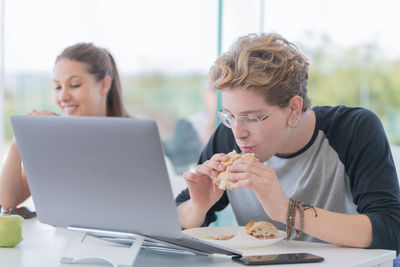 Man having food while sitting with friend by laptop at restaurant table 