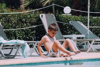 Full length of shirtless boy sitting at poolside