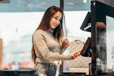 Young woman using phone while standing on laptop