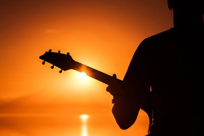 Close-up of silhouette man holding guitar against orange sky