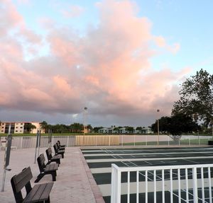 Empty benches on footpath by street against sky