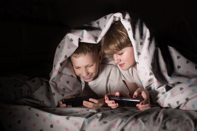 Lying under a blanket, hiding from parents, brother and sister