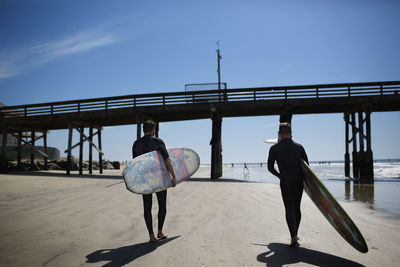 Rear view of men carrying surfboards at beach