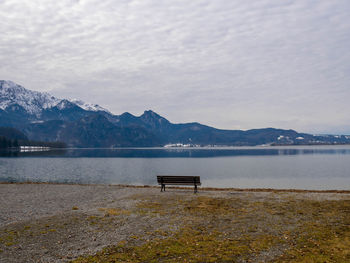 Empty bench by lake against sky