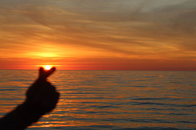 Silhouette person in sea against sky during sunset