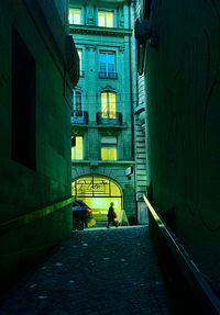 Rear view of man walking on footpath amidst buildings in city