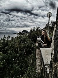 Woman sitting on stone wall by sea against sky