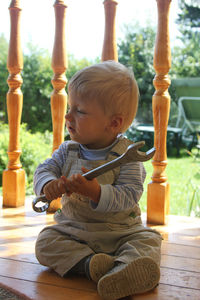 Full length of cute boy holding wrench sitting outdoors