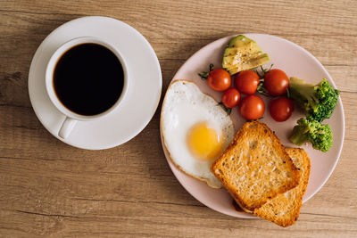 Breakfast with cup of black coffee, fried egg and toast with tomatoes and avocado on a plate	
