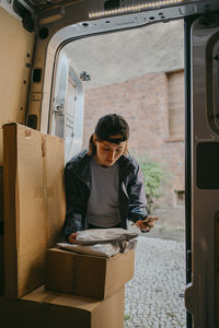 Female courier delivery person taking inventory of parcels while standing near van