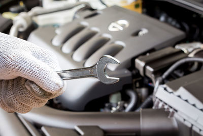 Cropped hand of mechanic holding wrench against car engine