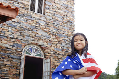 Portrait of smiling girl wearing american flag against building