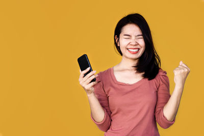 Smiling young woman using smart phone against yellow background