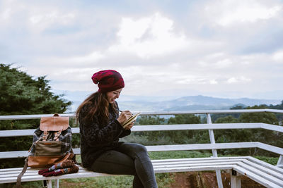 Woman sitting on railing against sky