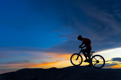 Silhouette man riding bicycle against sky during sunset