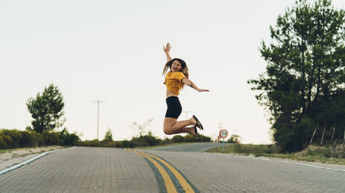 Young woman jumping on road against clear sky