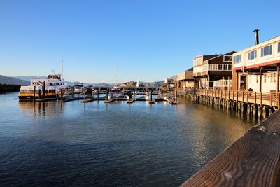 Sailboats moored on harbor by buildings in city against clear sky