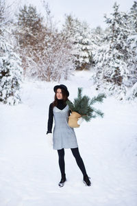 A girl in a silver dress and hat stands with her back in the middle of a beautiful winter forest.