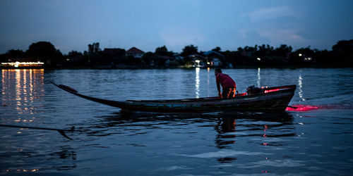 Silhouette man in boat on lake against sky
