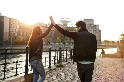 Germany, berlin, young walking along river spree high fiving