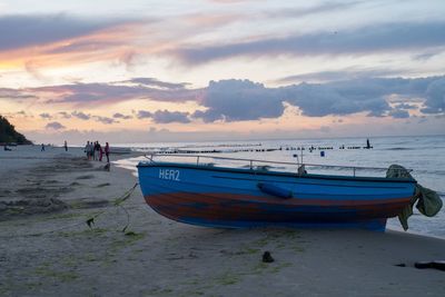 Boat moored on beach against sky during sunset