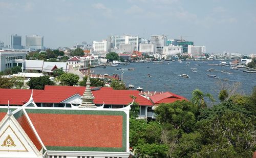 Temple in city by chao phraya delta river against sky