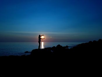 Silhouette woman standing on rock at beach against sky