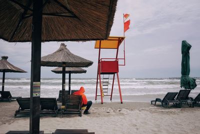 Person sitting on lounge chair at beach against sky