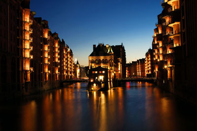 Illuminated buildings by river against sky at night