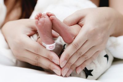 Cropped hands of mother holding baby feet while making heart shape with fingers